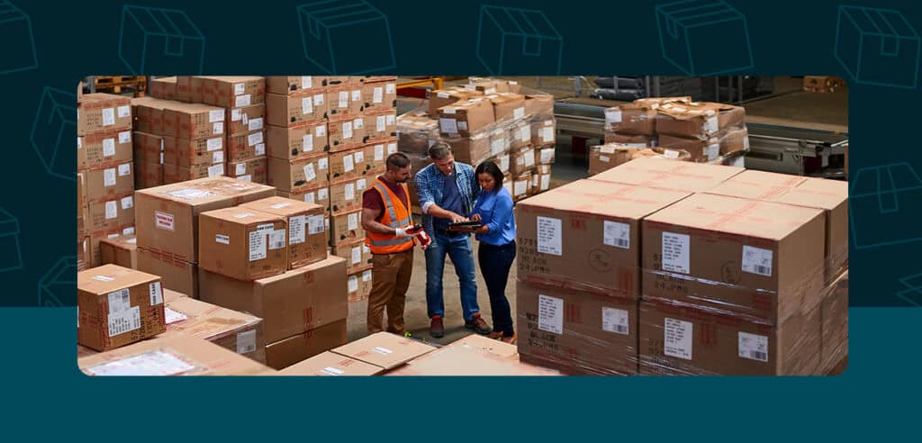3 workers in a warehouse surrounded by cardboard boxes
